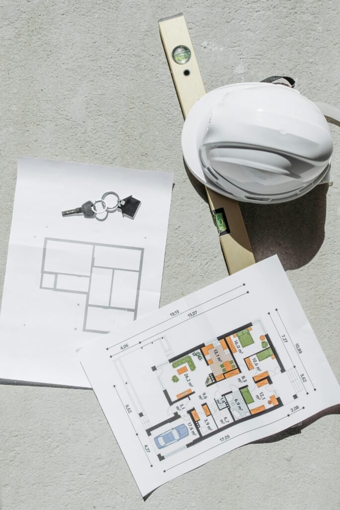 pexels-photo-7937323-7937323 Flat lay of construction plans, keys, hard hat, and level tool on concrete.